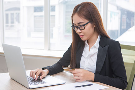 Side view of a young employee wearing glasses working in front of her laptop.