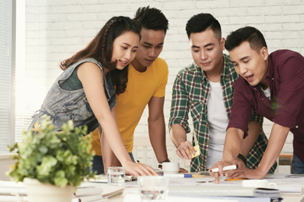 group young asian colleagues standing around table looking something